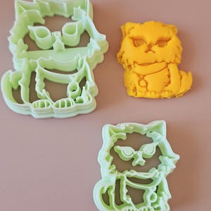 May include: Three cookie cutters shaped like cats. One is yellow and the other two are light green.