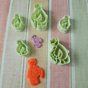 May include: Set of six green plastic cookie cutters shaped like different animals, including a bear, a bird, and a fish. There is also a single orange plastic cookie cutter shaped like a bear.