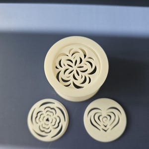 May include: Three white plastic cookie cutters, one in the shape of a flower, one in the shape of a heart, and one in the shape of a rose.