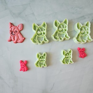 May include: Set of seven green and pink plastic cookie cutters shaped like French Bulldogs. The cutters are in various sizes.