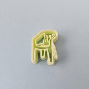 Peut inclure: Un emporte-pièce en plastique vert clair en forme de chaise. Le découpoir a un design simple et stylisé avec un dossier, une assise et des pieds. Le découpoir est sur une surface bleu clair.