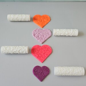 May include: Four white rolling pins with different embossed patterns and four heart-shaped pieces of fondant with matching patterns in orange, pink, red, and purple.