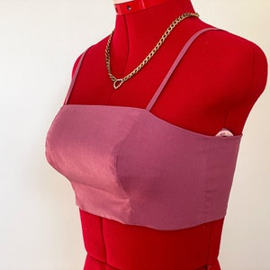 May include: A mauve crop top with thin straps. The top is made of a smooth, silky fabric.
