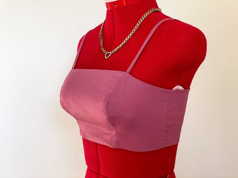 May include: A mauve crop top with thin straps. The top is made of a smooth, silky fabric.