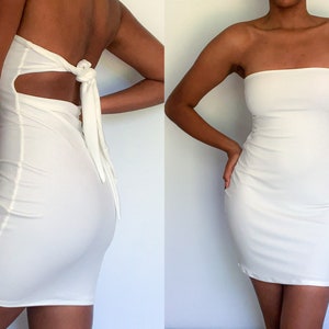 May include: A white strapless mini dress with a fitted silhouette. The dress has a cutout detail in the back and a tie closure.
