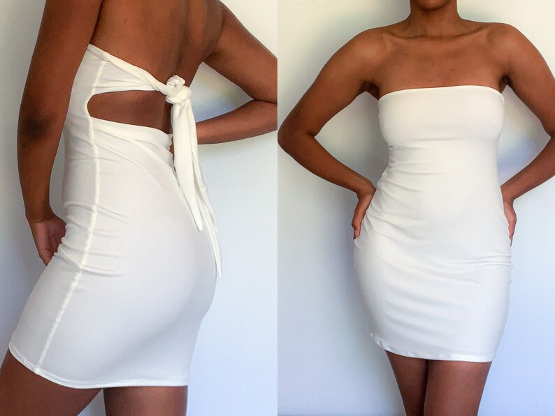 May include: A white strapless mini dress with a fitted silhouette. The dress has a cutout detail in the back and a tie closure.