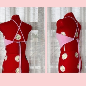 May include: A pink halter top with a criss-cross back and tie closure. The top is displayed on a red mannequin.