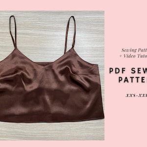 May include: A brown satin camisole top with thin straps. The top has a V-neck design and is displayed on a light wood surface. Text on the right side reads "Sewing Pattern + Video Tutorial" and "PDF SEWING PATTERN" with size range XXS-XXL.