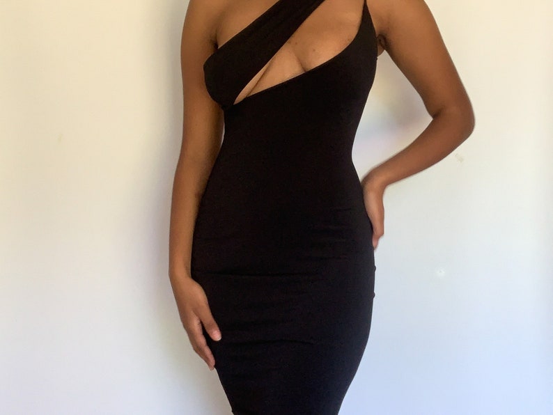 May include: A black, one-shoulder dress with a cutout detail. The dress has a fitted silhouette and a thin strap on one shoulder. The fabric appears to be a smooth, stretchy material.