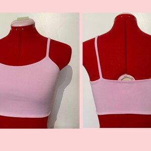 May include: A pink, sleeveless crop top with a scoop neck. The top is on a red dress form.