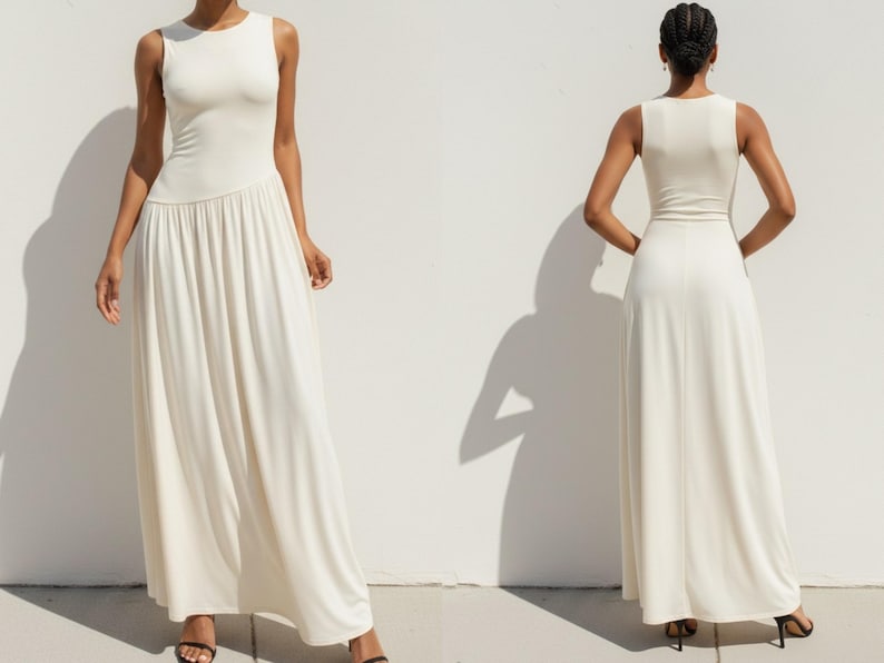 Puede incluir: Un vestido largo sin mangas de color marfil. El corpi&ntilde;o es entallado y se transforma en una falda plisada. El vestido tiene un escote redondo y una cintura definida. La modelo lleva sandalias negras. El vestido est&aacute; hecho de una tela suave y fluida.