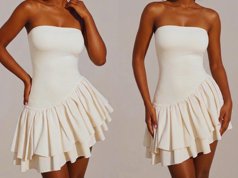 May include: Off-white strapless dress with a fitted bodice and a layered, ruffled skirt. The dress has a simple, elegant design, perfect for a special occasion. The fabric appears to be a soft, flowing material.