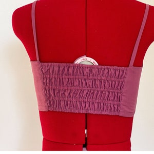 May include: A mauve-colored, strapless, cropped top with a gathered elastic band at the bust. The top has thin adjustable straps.