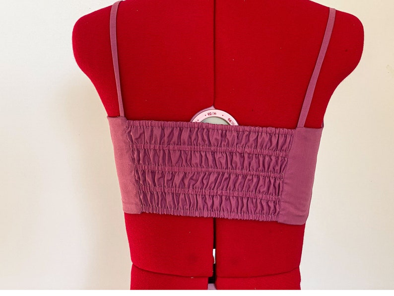 May include: A mauve-colored, strapless, cropped top with a gathered elastic band at the bust. The top has thin adjustable straps.
