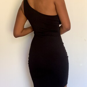 May include: A black, one-shoulder dress. The dress is form-fitting and ruched on the side. The dress is knee-length and made of a stretchy material.