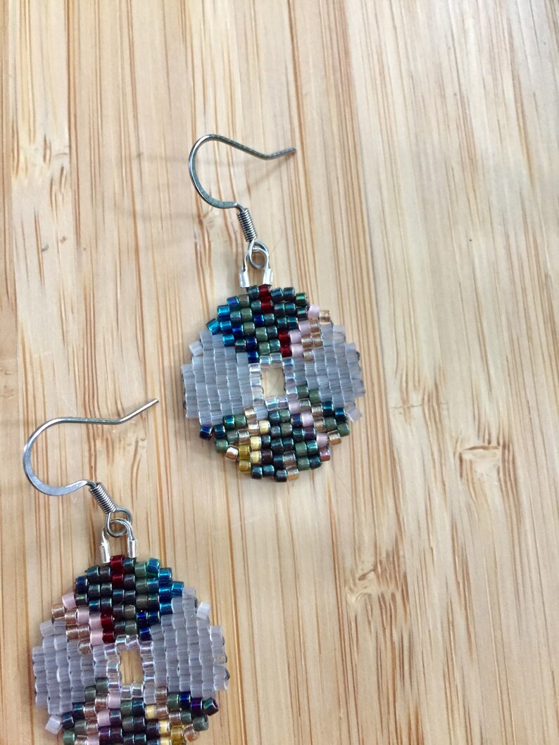 May include: A pair of silver hoop earrings with a beaded design. The beads are in shades of blue, green, gold, and red. The earrings are on a wooden surface.