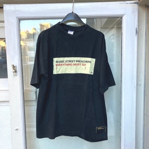 May include: Black t-shirt with a white rectangular patch that says "Manic Street Preachers Everything Must Go" in red text.