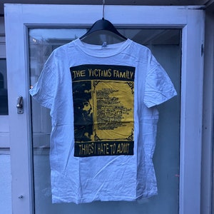 May include: White t-shirt with a yellow and black graphic print that says "The Victims Family" and "Things I Hate To Admit".