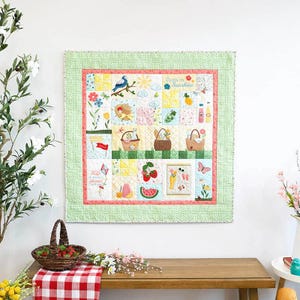 May include: A square wall quilt featuring a patchwork design with picnic-themed motifs including baskets, fruit, flowers, and a blue bird. The quilt has a green polka-dot border and includes the embroidered text "Sippin on Sunshine" and "Life is always a picnic".