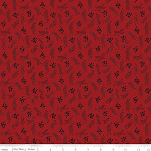 May include: A red fabric featuring a repeating pattern of small black floral motifs and clusters of thin, curved black lines. A white ruler at the bottom edge shows a scale of 12 inches, indicating the fabric's repeating design elements.