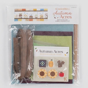 Könnte beinhalten: Ein Kimberbell Autumn Acres Kissen-Verzierungsset in transparenter Kunststoffverpackung. Das Set enthält einen braunen Reißverschluss, Filzbögen in Blau, Grün und Violett sowie eine Karte mit sechs Knöpfen in Form eines Quiltblocks, Kürbis, Eichhörnchens, zwei Sonnenblumen und eines Apfels.