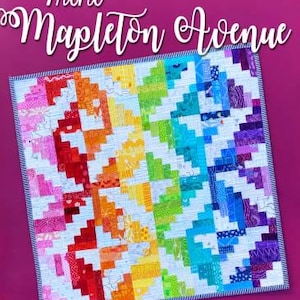 May include: Mini Mapleton Avenue quilt with a rainbow pattern. The quilt is made of colorful fabric squares and is bordered with a white and blue trim.
