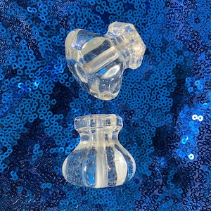 Puede incluir: Dos tapones de botella de vidrio transparente con un diseño texturizado. Los tapones están sobre un fondo azul brillante.