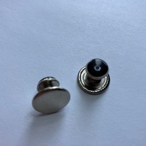 May include: Two silver metal button snaps with a black center. One snap has a flat top and the other has a raised dome.