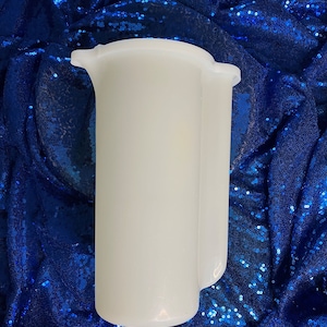 May include: A white plastic pitcher with a handle. The pitcher is on a blue sequined background.