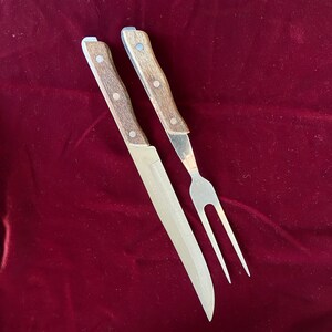 Peut inclure: Un ensemble de deux couteaux de cuisine avec des manches en bois. Le couteau de gauche est un couteau à découper avec une lame longue et fine. Le couteau de droite est une fourchette avec une lame plus courte et plus épaisse.