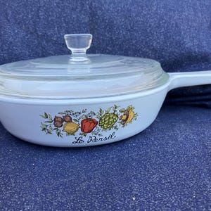 May include: White casserole dish with a glass lid and handle. The dish features a colorful vegetable design with the text "Le Persil" on the front. The lid has a clear knob.