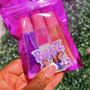 May include: A pink zippered pouch with three clear lip gloss tubes. The lip glosses have glitter and are labeled with the word "Bratz".