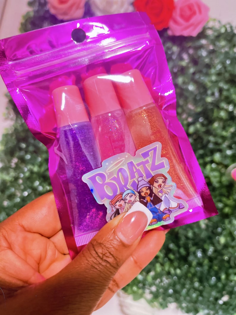 May include: A pink zippered pouch with three clear lip gloss tubes. The lip glosses have glitter and are labeled with the word "Bratz".