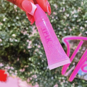 May include: A pink lip gloss tube with a clear, glittery gloss inside. The tube has the word "IPLK" printed on it in white letters.