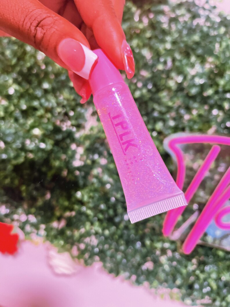 May include: A pink lip gloss tube with a clear, glittery gloss inside. The tube has the word "IPLK" printed on it in white letters.