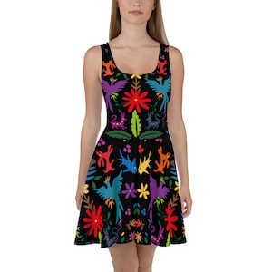 Puede incluir: Un vestido negro sin mangas de estilo skater con un estampado de arte popular mexicano colorido que presenta pájaros, flores y diseños geométricos.
