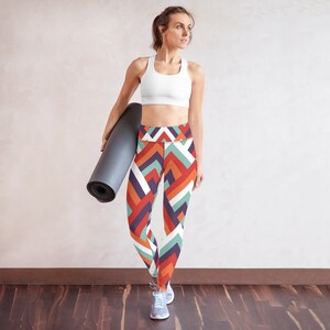 Puede incluir: Una mujer con un sujetador deportivo blanco y leggings con estampado geométrico de colores sostiene una esterilla de yoga negra.