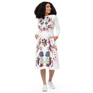 Puede incluir: Vestido blanco de manga larga con un estampado floral colorido. El vestido tiene un escote redondo y bolsillos a los lados.