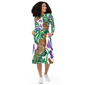 May include: A long-sleeved dress featuring a vibrant print of brown birds, green leaves, and purple flowers on a white background. The dress has a midi length and pockets. The model is wearing white sneakers.