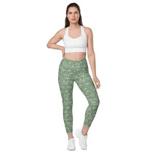 May include: Green leggings with a white abstract face pattern. The leggings are fitted and have a high waist.