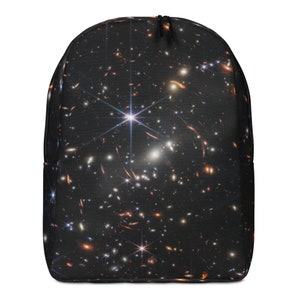 Puede incluir: Una mochila negra con estampado de galaxia con fondo azul oscuro con estrellas blancas, naranjas y azules.