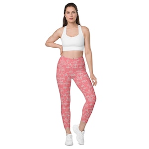 May include: Coral pink leggings with a white abstract face pattern. The leggings are cropped and have a high waist.