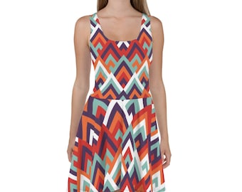 Puede incluir: Un vestido skater sin mangas con un patrón geométrico en tonos naranja, rojo, blanco, azul y morado. El patrón está formado por formas repetidas que crean un efecto de chevron.