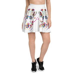 Puede incluir: Una falda skater blanca con un estampado floral colorido que presenta mariposas y pájaros. La falda tiene una cintura ancha y una silueta acampanada.