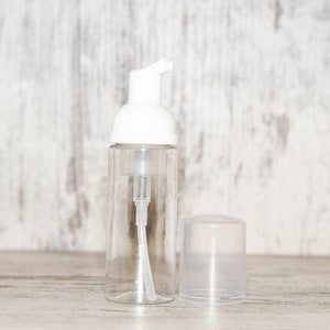 May include: A clear glass bottle with a white foam pump top and a separate clear plastic cap. The bottle is empty and ready to be filled with liquid soap or lotion.
