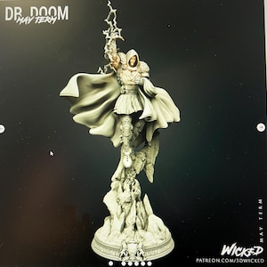 May include: A detailed figurine of Dr. Doom, holding a lightning bolt, with a flowing cape. The figure is standing on a rocky base with intricate details. The text "DR. DOOM MAY TERM" is visible at the top left. The word "Wicked" and a website address are at the bottom right.
