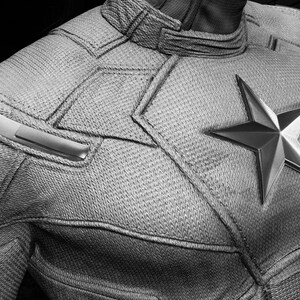 May include: Close-up of a Captain America costume in grayscale. The costume features a large, metallic star emblem on the chest and textured fabric. The words "Avengers Assemble" are visible in the upper left corner.