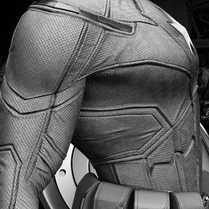 May include: Black and white image of a superhero costume, featuring textured fabric and geometric paneling. The costume includes a utility belt and a portion of a shield. The words "Avengers Assemble" are visible in the upper left corner.