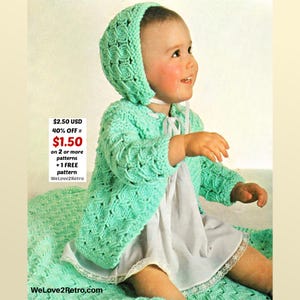 May include: A baby wearing a mint green knitted hooded jacket and matching bonnet. The jacket has a textured pattern and a white ribbon closure. The baby is also wearing a white dress. The image includes the text "WeLove2Retro.com".