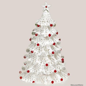 May include: A white crocheted Christmas tree ornament featuring a star topper and decorated with small red and clear spherical beads throughout the tiered, open-work fabric structure. The base of the tree is wide, tapering to a point at the top.